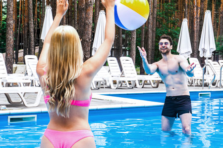 Happy couple standing in the swimming pool while playing with inflatable ball, enjoying the weekend....