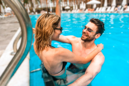 Romantic couple in sunglasses enjoying each other company in a holiday resort swimming pool. Romance and summer vacation conceptの写真素材