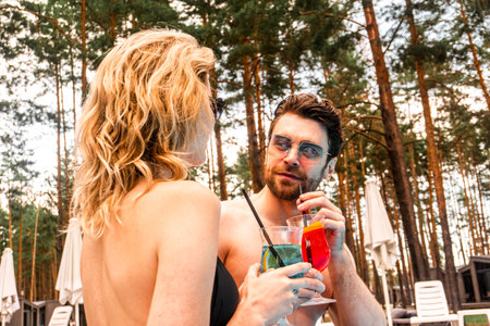 Cute guy sipping a glass of cocktail in his girlfriend company in the recreation area. Rest and relaxation conceptの写真素材