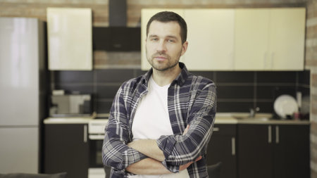Confident man in checkered shirt standing on kitchen, looking at cameraの写真素材