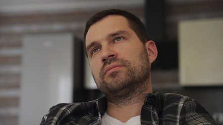Thoughtful young bearded man sitting at home while watching tv. Slow motionの写真素材