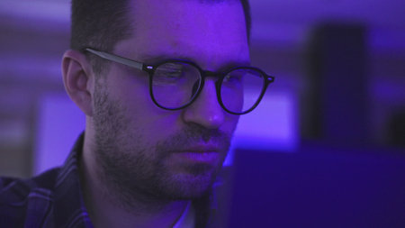 Young man trader wearing glasses looking at computer screen with trading chartsの写真素材