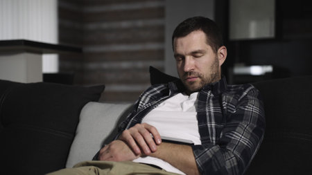 Tired Caucasian guy napping on sofa at home, holding smartphone. Slow motionの写真素材
