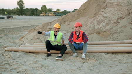 Two construction workers discussing, sitting near sand