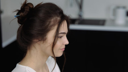 Young woman in kitchen during quarantine. Girl sits at table and works on laptop. Typing on its keyboard. Camera moves down from girl's head to her hands. Work from home remote.の写真素材