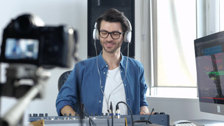 Young man in sound recording studio. Guy video blogger greets and start using music mixing console. Show how to work with professional sound equipment.の写真素材