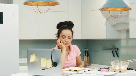 Young woman working at home during quarantine. Tired exhausted girl get headphones and start talking with joy and smile. Working online from home. End of day after cooking.の写真素材