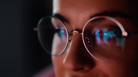 Young woman at home during quarantine. Close up of a girl's face looking at a screen with its reflection. Watching a video or movie late at night.の写真素材