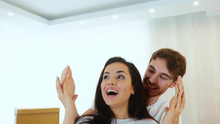 Young couple move into new apartment. Slow motion of woman stand with closed eyes. Camera moves backwards. Guy open womans eyes and showing new apartment. Happy cheerful woman expressing.の写真素材