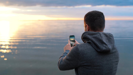 a man photographs the sunset or takes a video on the sea on the phoneの写真素材