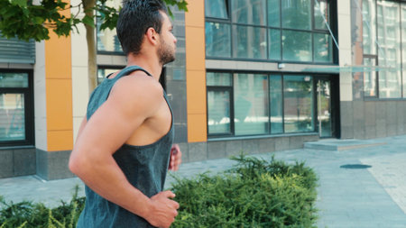 Young man exercising outside. Back side view slow motion of strong enduring powerful guy jogging or slow running alone on street. Training in morning or evening. Exercise for athlets.の写真素材