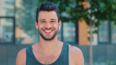 Young man exercising outside. Positive happy cheerful guy listen to music in earphones and smile. Posing no camera. Happiness in mans eyes and face.の写真素材