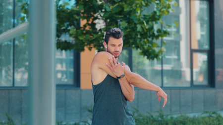 Young man exercising outside. Guy warming up his upper body and stretching it before workout. Leaning to sides and take care of health. Exercising alone.の写真素材