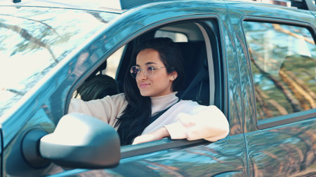 Young woman sit in car during travelling break. Girl in forest sitting inside and unbuckle the seat belt an open cars door to go outside. Happy positive girl on video.の写真素材