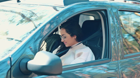 Young woman sits in car during travelling break. Girl eats lunch alone inside. Woman devours burger and drinks hot from thermos. Tasty delicious meal.の写真素材