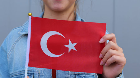 Caucasian teenage girl in red t-shirt and denim jacket keeping small flag of Turkey in her hands....