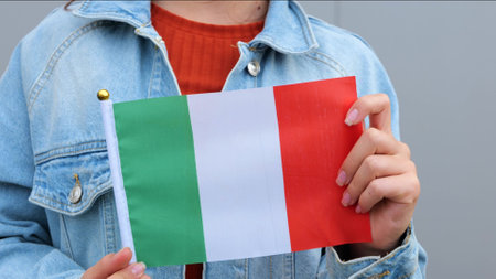 Caucasian teenage girl is keeping small flag of Italy in her hands. Young female is smiling and waving small Italian flag in her hands.の写真素材