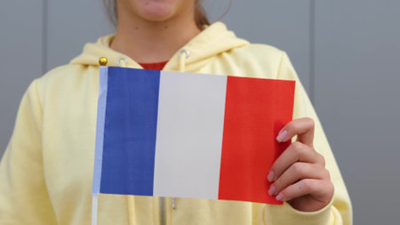 Female small girl in yellow hoodie, keeping flag of France in her hands. Beautiful Caucasian Young teenage Girl waving small French flag, smiling at camera.の写真素材