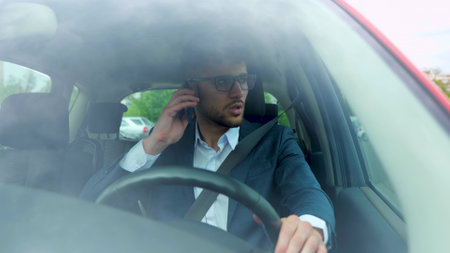 Businessman talking on mobile phone while driving and overtaking, paying attention to the road. Transport, business, technology and people concept. Slow motionの写真素材