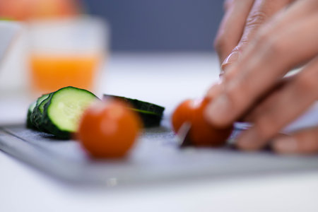 Close up shot of female hands preparing breakfast in kitchen using knife. Woman slicing fresh cucumbers and tomatoes on cutting board making a salad indoor. Food conceptの写真素材