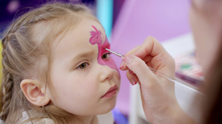 Female professional artist applying make up drawing unicorn on face for little girl, close up. Photography, creative process. Slow motion. Childhood, art, creative conceptの写真素材