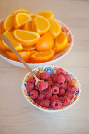 Little raspberries bowl with a spoon and a big oranges.の写真素材
