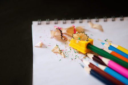 Colored pencils, sharpener and shavings on a notepad on a black background