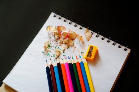 Colored pencils, sharpener and shavings on a notepad on a black background