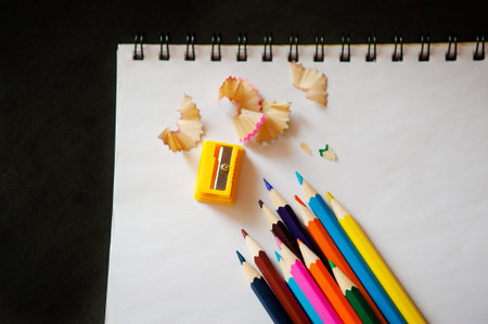 sharpened colored pencils, sharpener and shavings on a white notebook
