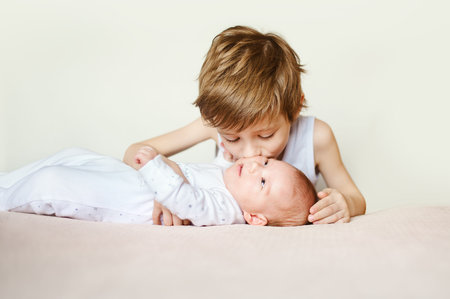 baby in white pajamas lying on his back. Older brother kisses his. bright portraitの写真素材