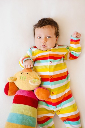 Cute baby with Striped colored pajamas and a striped cat toy lying on bed. Flat layの写真素材