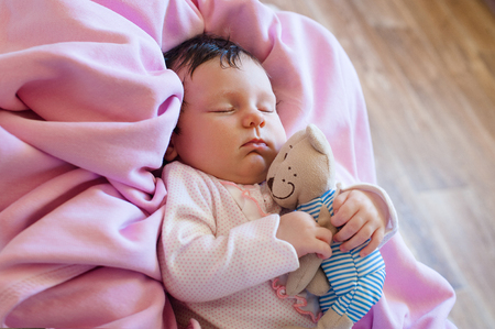 Cute newborn baby sleeps with a toy teddy bearの写真素材