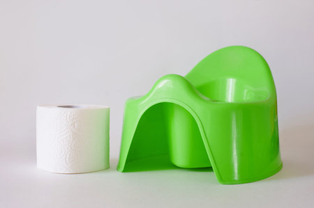White toilet paper and stack of diapers beside green potty on white background
