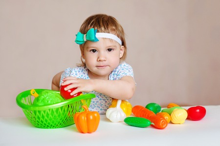 Kid having a table full of plastic food. Cheerful toddler eating healthy salad and fruits.の写真素材