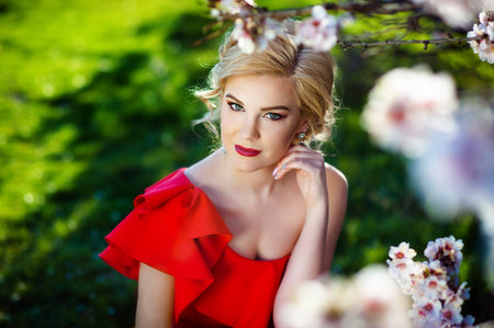 Beautiful young woman with With long hair gathered in a styling posing near blossoming spring tree in a garden. The concept of perfume advertising.の写真素材