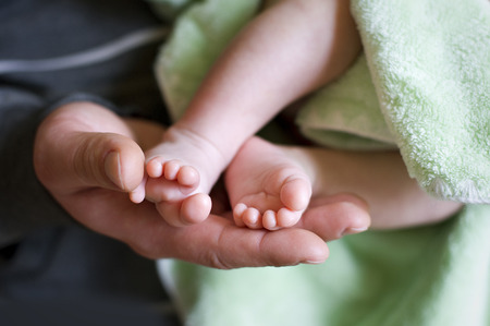 Baby in fathers hands. Both parents support childs feet with his hands. Close up.の写真素材