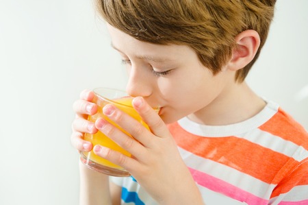 Young beautiful caucasian boy drinking orange juice from glassの写真素材