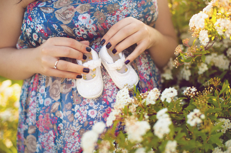 Closeup of pregnant woman holding baby shoes on her bellyの写真素材