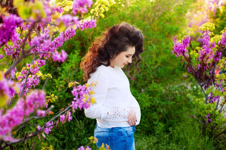 Pregnant happy girl in blossom pink garden