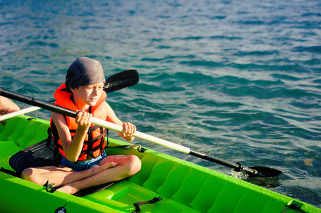 A teenage boy paddling a kayak on a lake. There is a fishing pole in the kayak with him.の写真素材