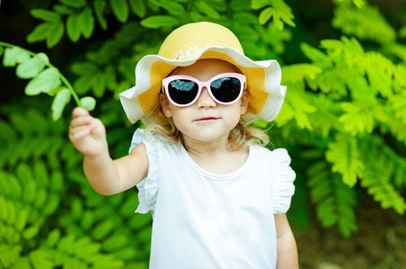Cute little girl on the meadow in spring day. Cute little girl is playing with leaves in summer parkの写真素材