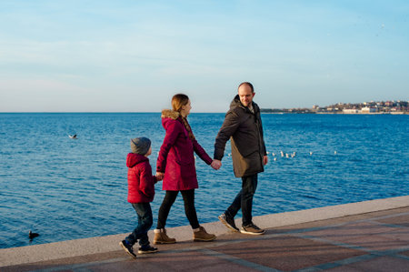 Happy young caucasian family with five year old son walking along stony jetty on sunshine, back view. Happy family concept with copy space or text on left areaの写真素材