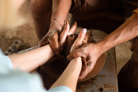 Closeup hands of the potter and his young apprentice create a vase on a spinning potters wheelの写真素材