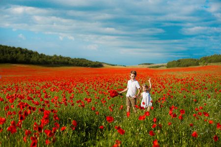 girl and boy in a field of red poppies. concept of childhood, happiness, familyの写真素材