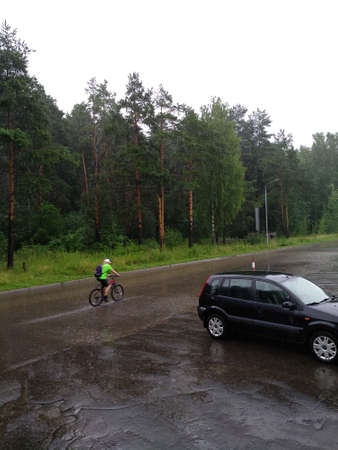 A cyclist in a green jersey rides along a wet park path in the rain.のeditorial素材