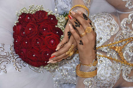 bride's hands on red wedding bouquet of flowers, details of white dress and gold wedding ring. High quality photoの写真素材