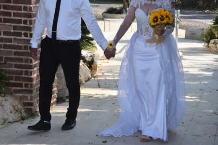 Newlyweds bride and groom in white with a bouquet of yellow sunflowers flowers. High quality photoの写真素材