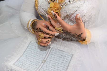 the bride's hand with gold rings, a bracelet and henna drawing on the skin, muslim wedding prayer book, a white wedding dress. High quality photoの写真素材