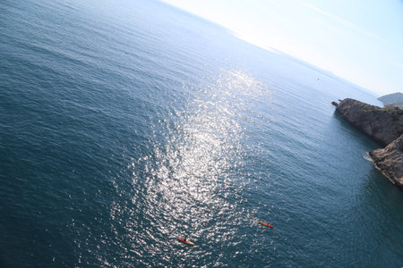 blue sea water, red yellow boat with oars floats, two people sport background Dubrovnik, Croatia April 22, 2023. High quality photoの写真素材