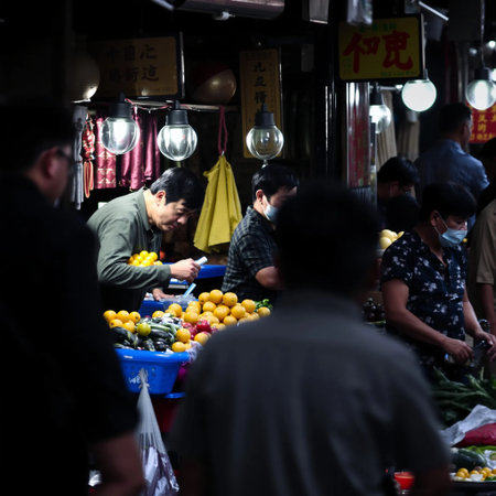 A street photo of a bustling market in an Asian city where vendors sell colorful fruits and vegetables. Use a shallow depth of field to focus on the vendors' expressions and interactions. High quality photoの写真素材